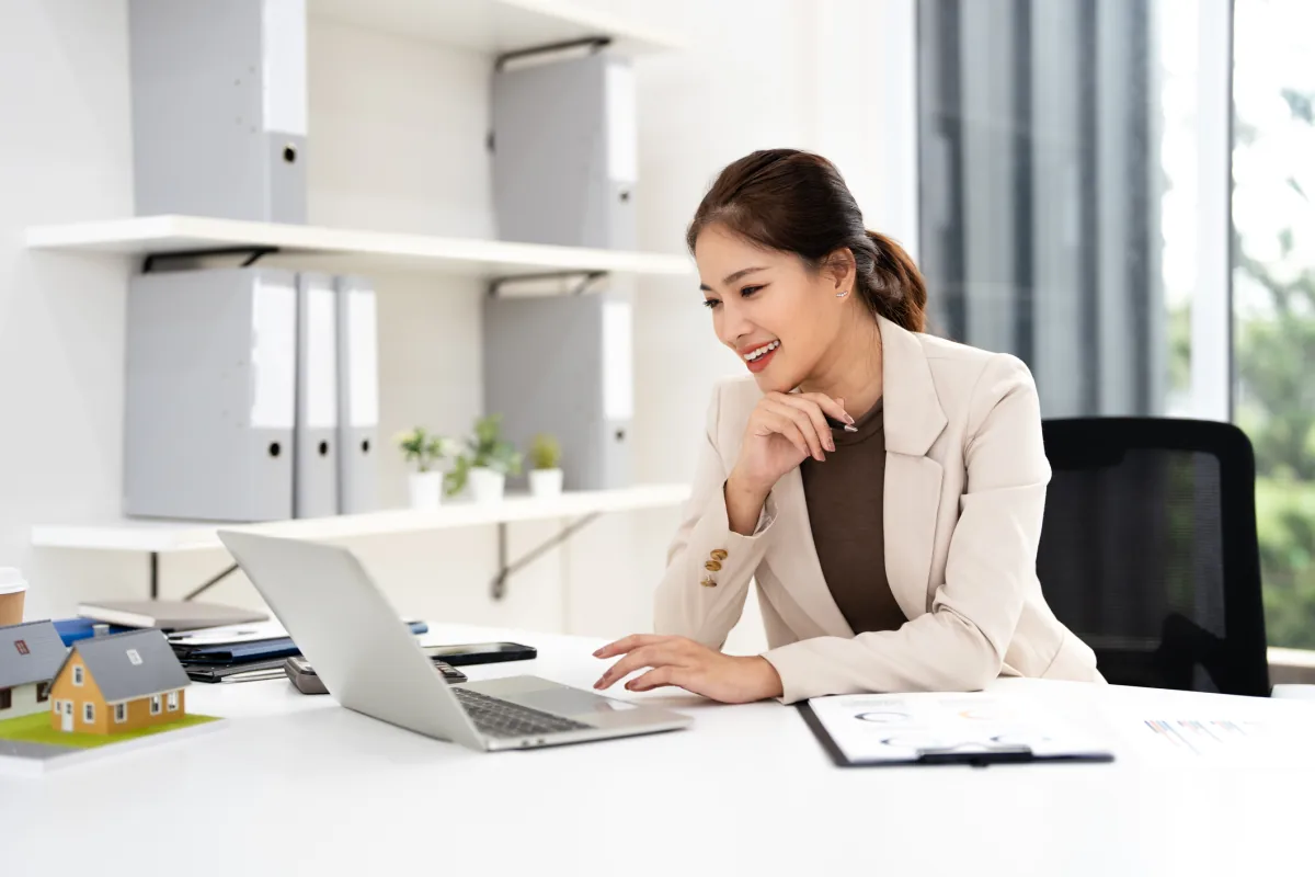 A real estate professional smiling while working at her laptop in a bright office